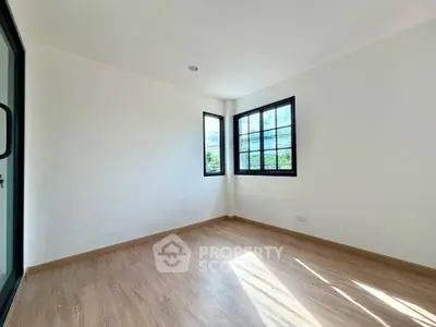 Bright empty room with wooden flooring and large windows offering natural light.