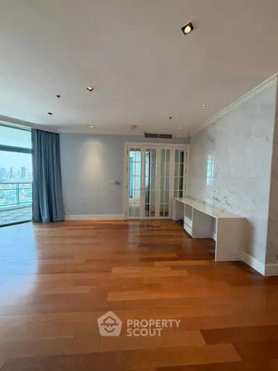 Spacious living room with hardwood floors and city view, featuring elegant French doors and modern lighting.