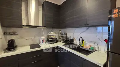 Modern kitchen with sleek dark cabinets and marble backsplash, featuring a built-in stovetop and stylish sink.