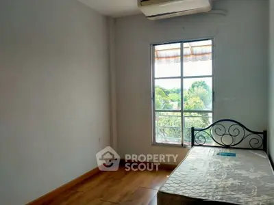 Cozy bedroom with natural light and scenic view, featuring a simple bed and wooden flooring.