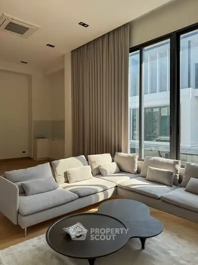 Spacious modern living room with large windows and stylish gray sectional sofa.