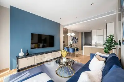 Modern living room with blue accents and open kitchen layout, featuring stylish decor and ample natural light.