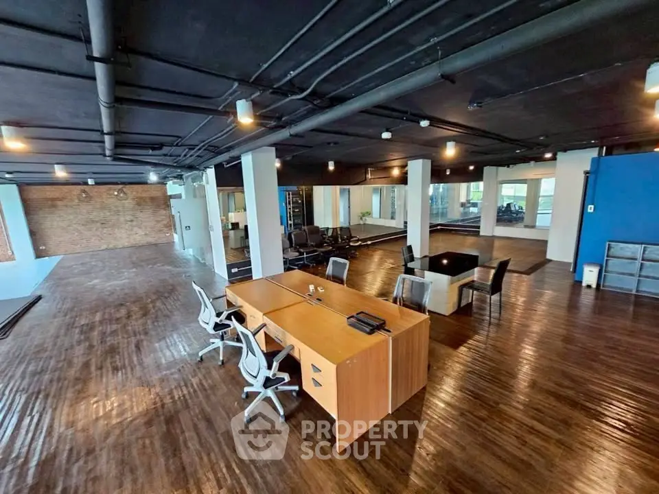 Spacious modern office space with sleek wooden flooring and stylish furniture, ideal for creative work environments.