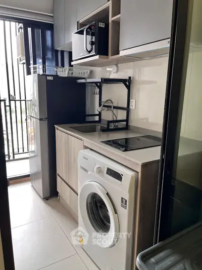 Modern kitchen with appliances including washing machine and fridge, sleek cabinetry, and balcony view.