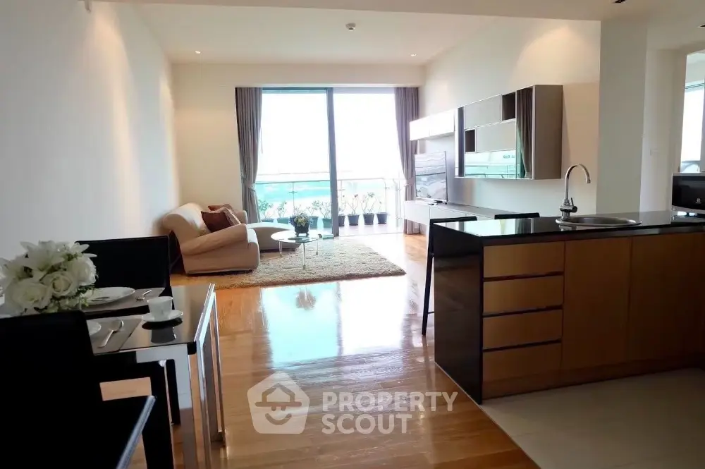 Modern open-plan living room with kitchen, featuring sleek furniture and large windows for natural light.