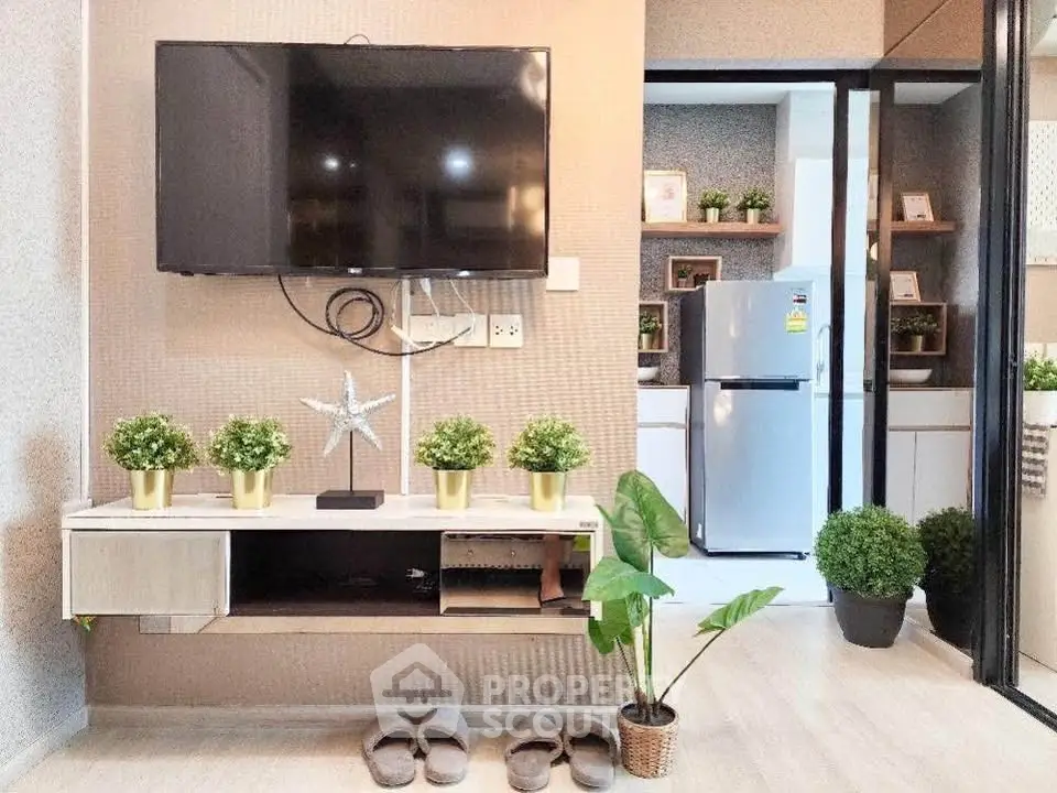 Modern living room with wall-mounted TV and stylish decor, leading to a sleek kitchen with stainless steel fridge.