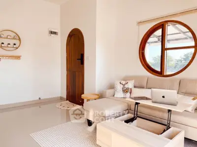 Charming living room with unique round window and cozy beige sofa, perfect for relaxation and work-from-home setup.