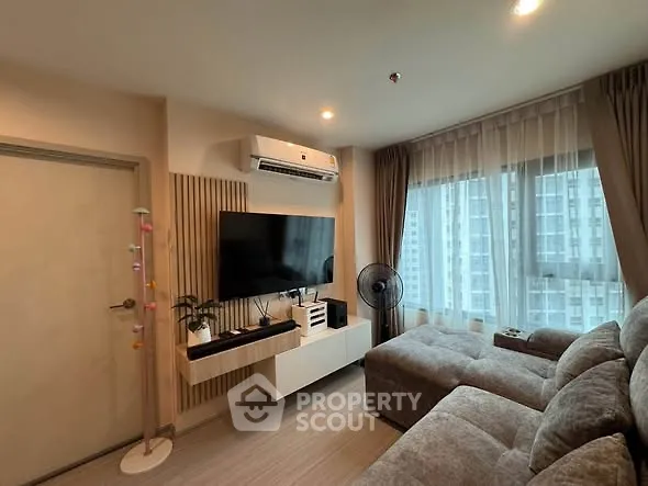 Modern living room with large TV, cozy sofa, and city view from window.