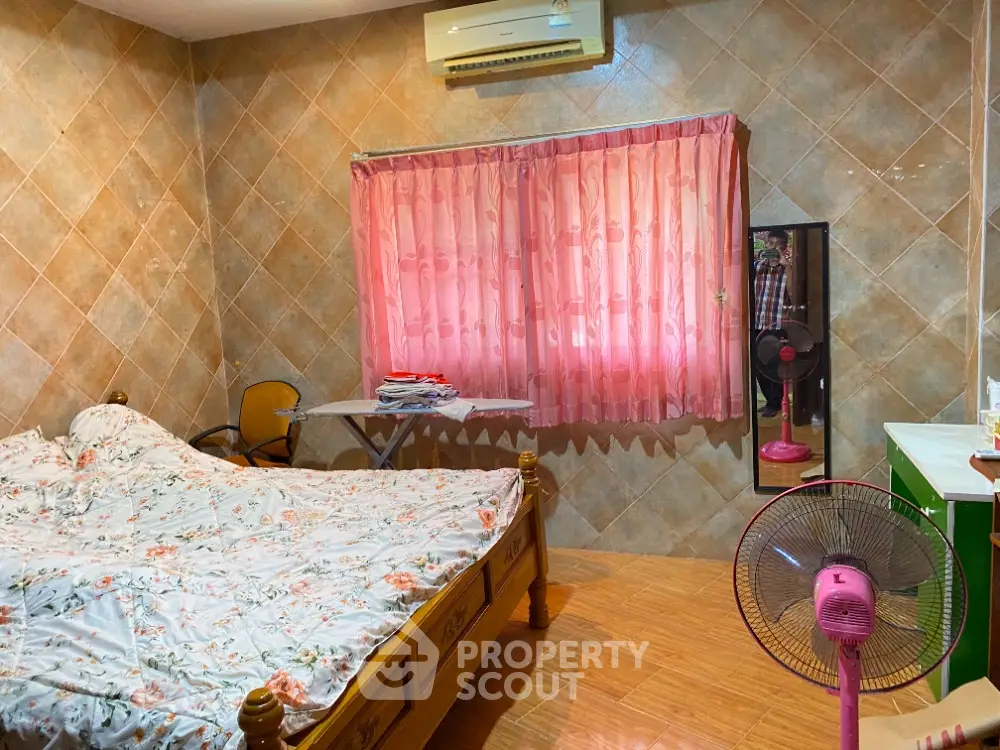 Cozy bedroom with floral bedding and pink curtains, featuring air conditioning and wooden furniture.