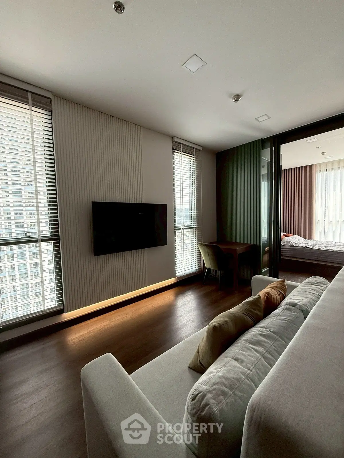 Modern living room with sleek design and large windows offering city views, adjacent to a cozy bedroom.