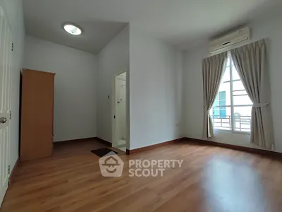 Spacious bedroom with wooden flooring and large window, featuring an air conditioner and wardrobe.
