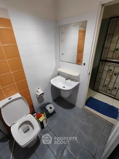 Compact bathroom with modern fixtures and tiled walls, featuring a sink, toilet, and mirror.