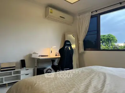 Cozy bedroom with study area and large window offering natural light and greenery view.