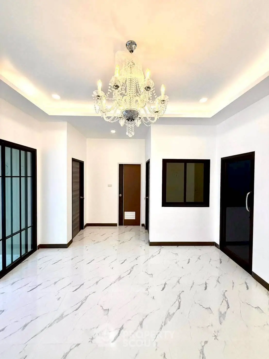 Elegant living room with marble flooring and chandelier, featuring modern black-framed doors.