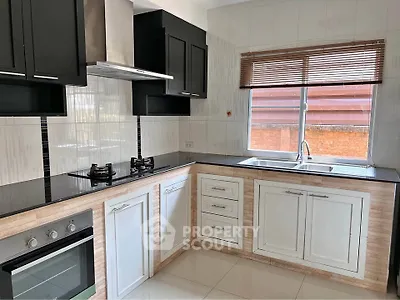 Modern kitchen with sleek black cabinets, gas stove, and large window for natural light.
