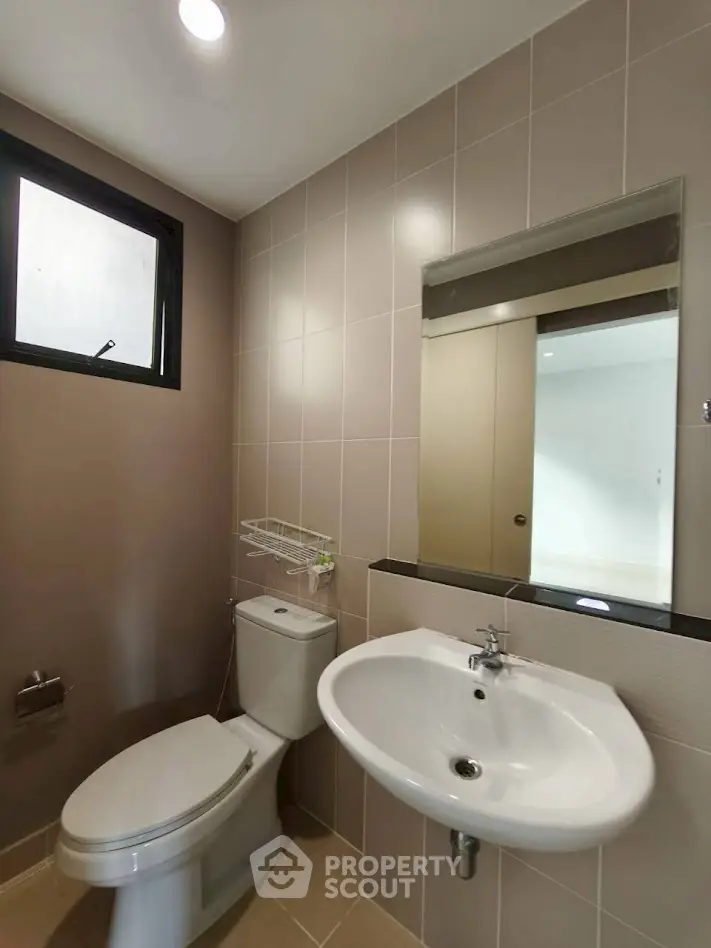 Modern bathroom with sleek fixtures and neutral tiles, featuring a large mirror and natural light.