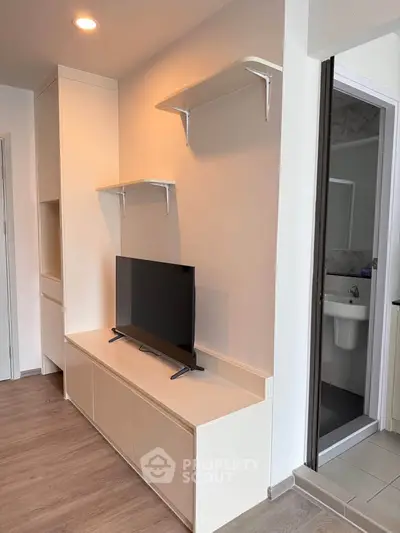 Modern living room with sleek TV unit and open shelves, adjacent to a bathroom entrance.