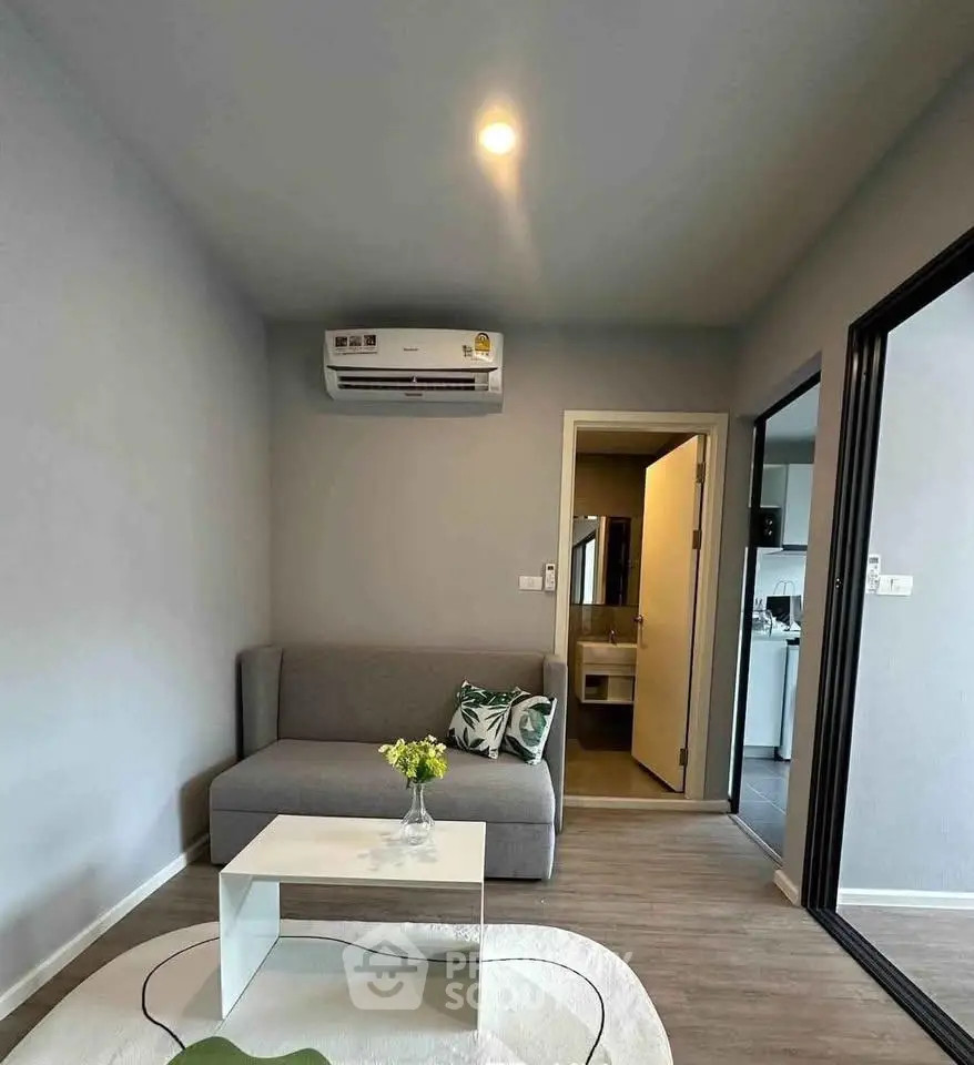 Modern living room with sleek design, featuring a cozy sofa, air conditioning, and a glimpse into the kitchen area.