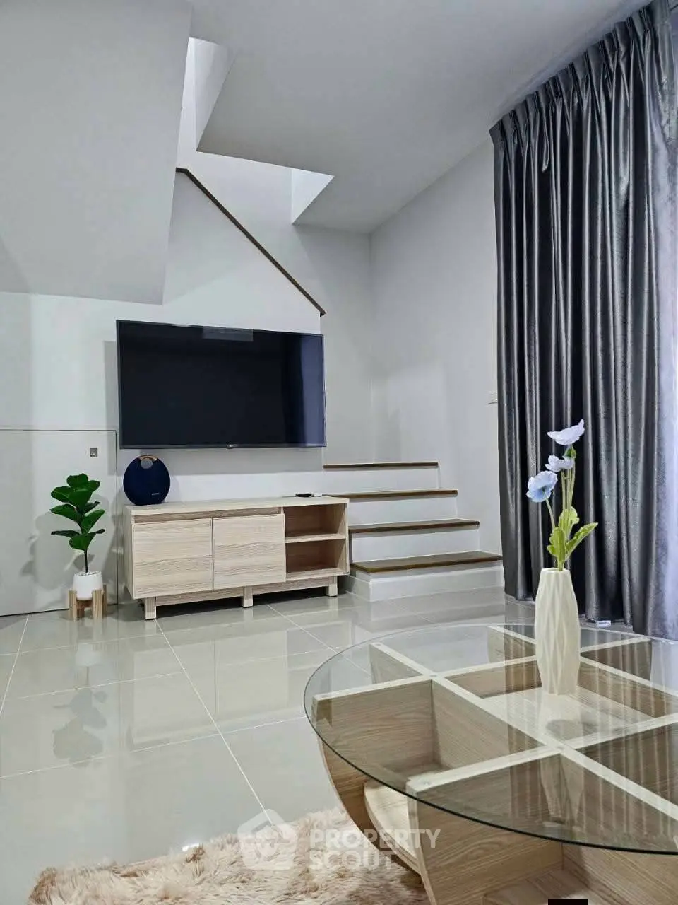 Modern living room with sleek furniture and stylish decor, featuring a glass coffee table and elegant staircase.