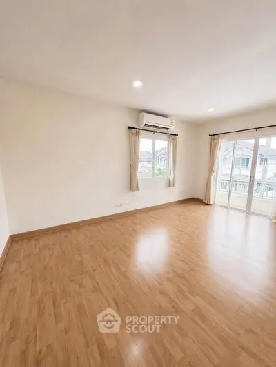 Spacious empty living room with wooden flooring and large windows for natural light.