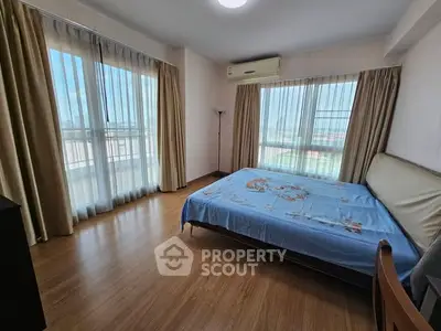 Spacious bedroom with large windows and wooden flooring, offering ample natural light and a serene atmosphere.