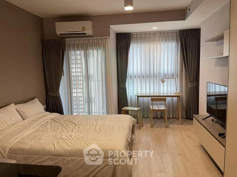 Modern bedroom with cozy decor, featuring a large window, desk, and TV unit, perfect for urban living.
