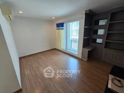 Spacious living room with wooden flooring and built-in shelves, featuring a large window for natural light.