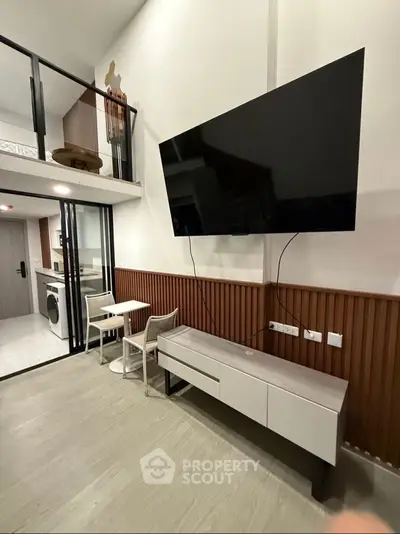 Modern living room with high ceiling, wall-mounted TV, and stylish furniture in a contemporary apartment.