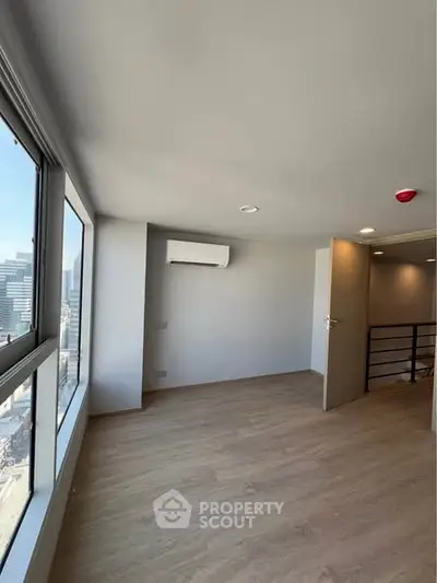 Spacious modern room with large windows and city view, featuring sleek wooden flooring and air conditioning.