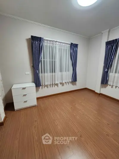 Spacious empty bedroom with wooden flooring and elegant curtains
