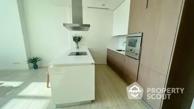 Modern kitchen with sleek wooden cabinetry and a central island under a contemporary extractor hood, complemented by built-in appliances and ample natural light.