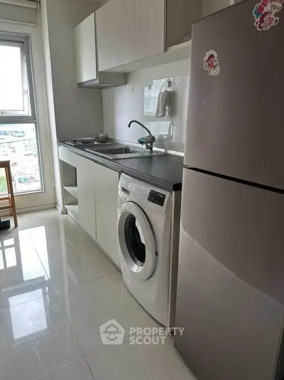 Modern kitchen with sleek appliances and city view, featuring washing machine and fridge.