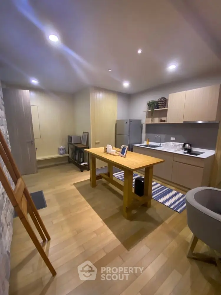 Modern kitchen with sleek cabinetry and wooden dining table in cozy apartment.