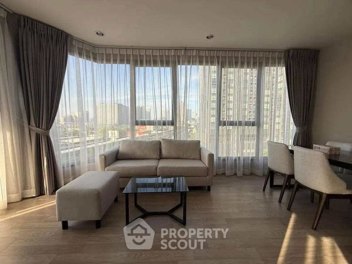 Spacious living room with large windows and modern furniture, offering a stunning city view.