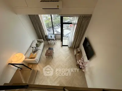 Modern loft living room with high ceiling and large windows offering natural light and a cozy ambiance.