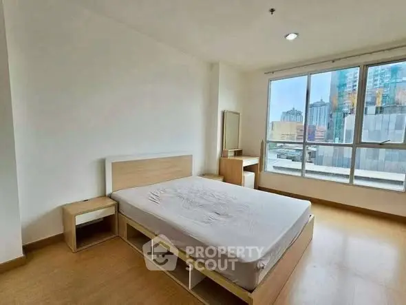 Spacious bedroom with large window offering city views, featuring modern wooden furniture.