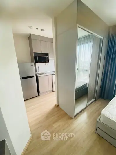 Modern apartment interior with compact kitchen and bedroom, featuring sleek appliances and natural light.