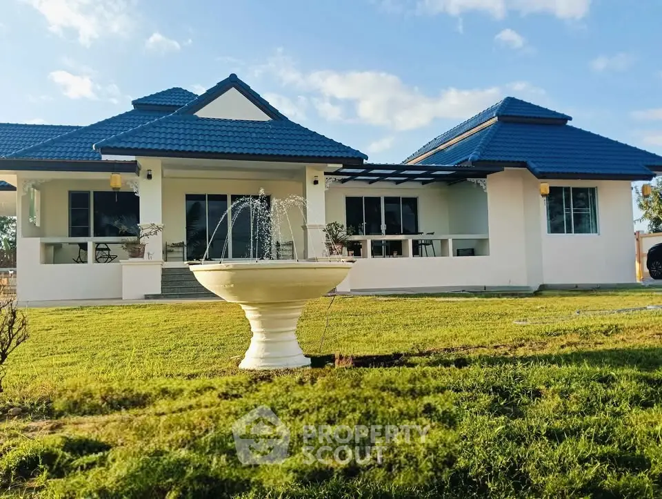 Charming single-story home with blue roof and elegant fountain in lush green yard.