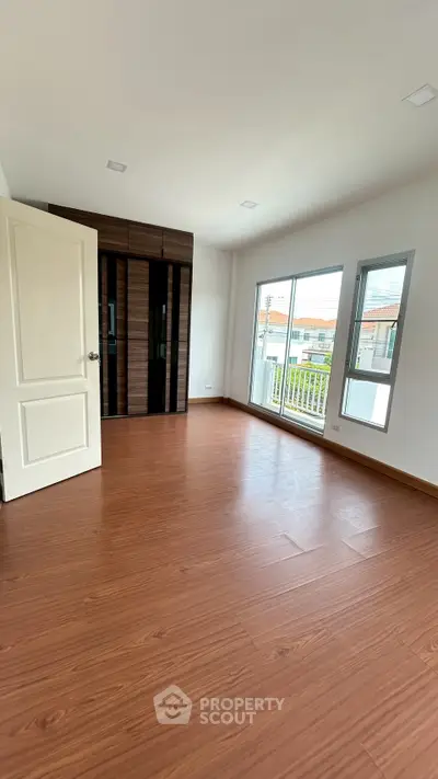 Spacious bedroom with wooden flooring and large windows offering natural light and a view.