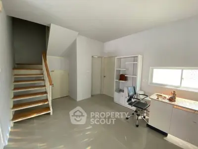 Spacious study room with modern desk and storage, featuring natural light and staircase access.
