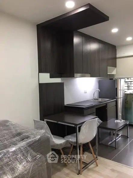 Modern kitchen with sleek dark cabinets and compact dining area in a stylish apartment.