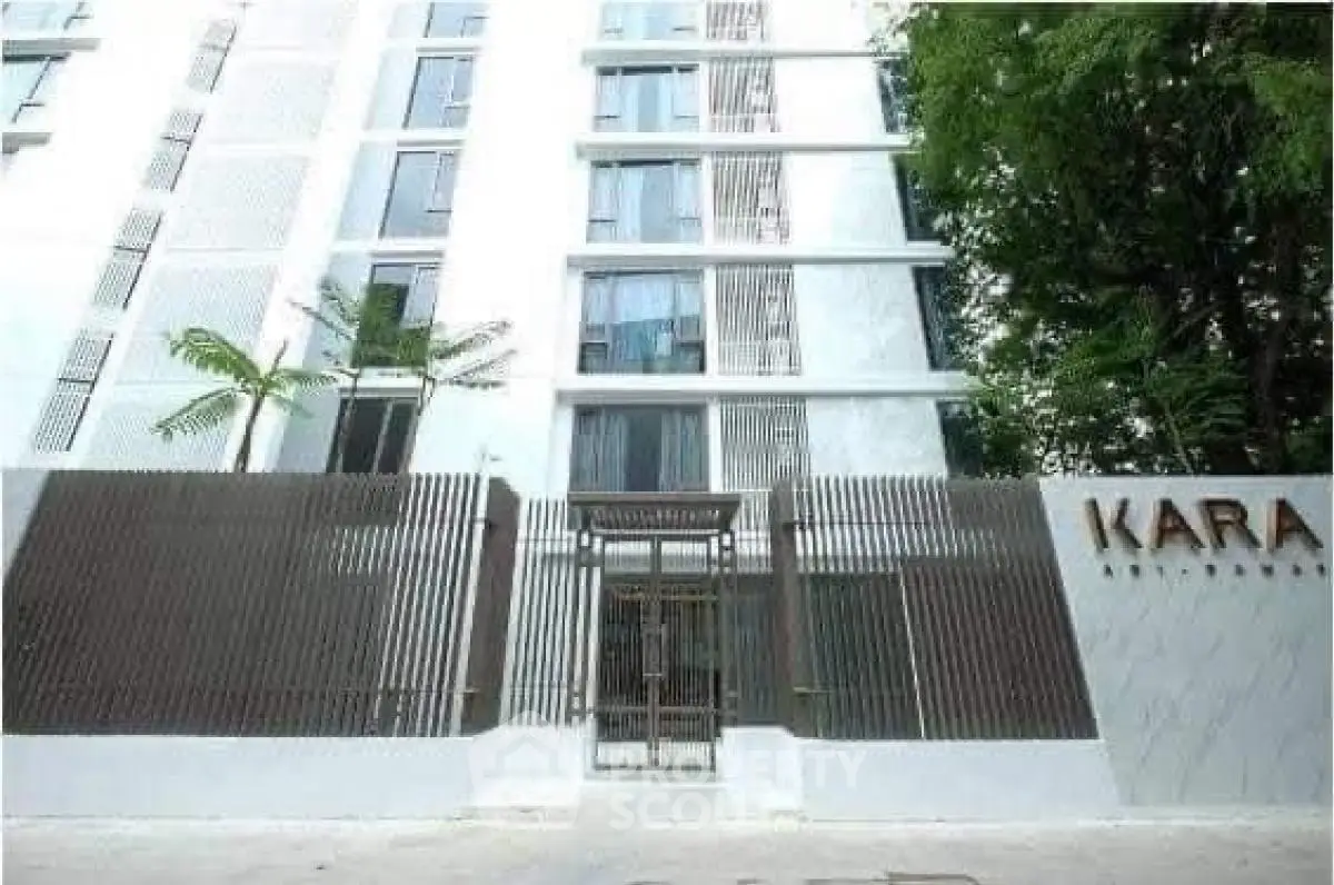 Modern apartment building with sleek design and gated entrance in lush surroundings.
