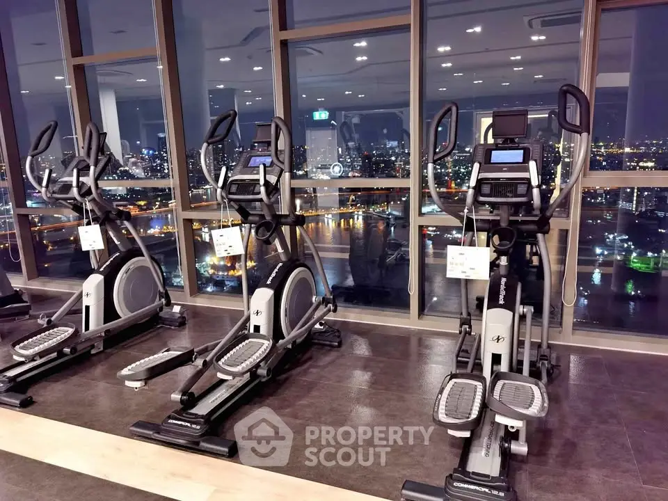 Luxurious high-rise gym with stunning city skyline view, featuring modern exercise equipment and floor-to-ceiling windows.
