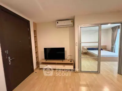 Modern apartment interior with wooden flooring, TV unit, and sliding door to bedroom.