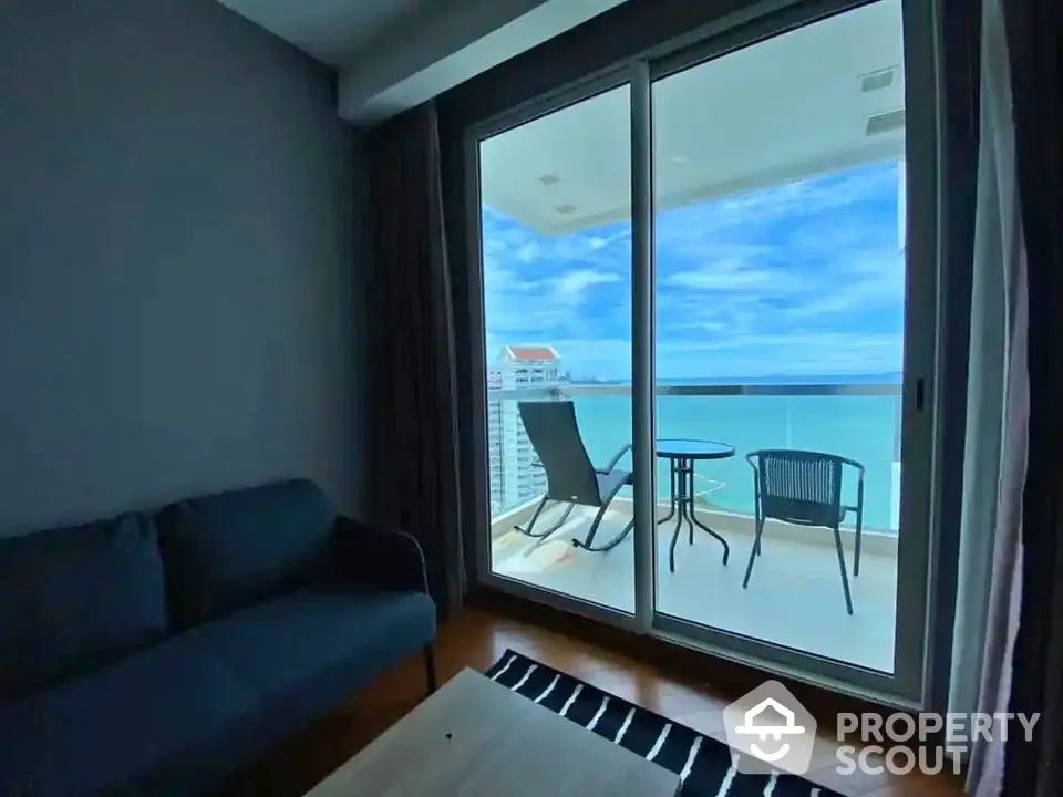 Stunning ocean view from modern apartment balcony with cozy seating area.