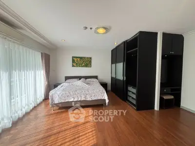 Spacious bedroom with wooden flooring and large windows in modern apartment.