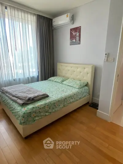 Cozy bedroom with natural light, wooden flooring, and modern air conditioning unit.