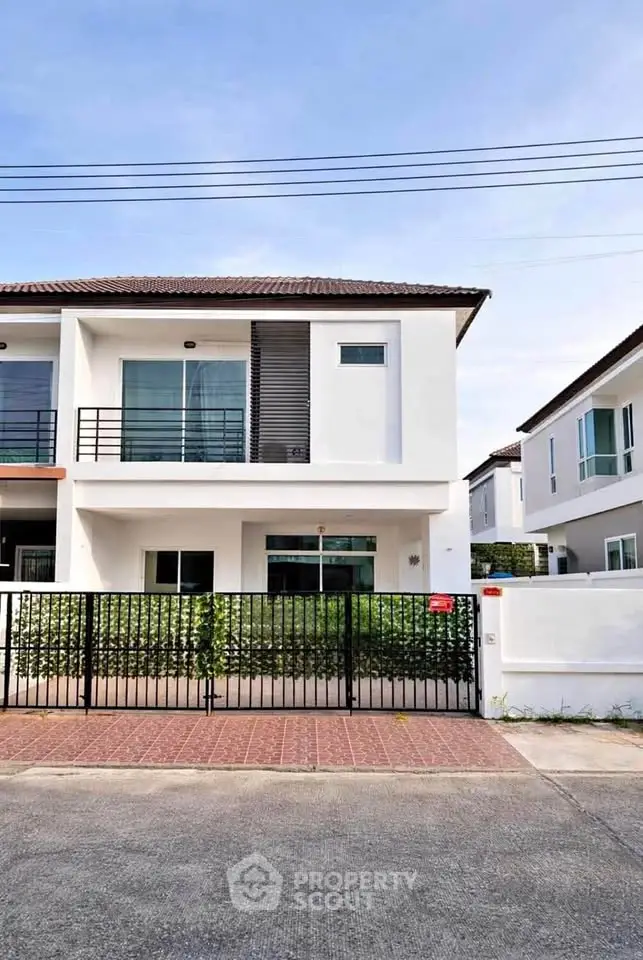 Modern two-story white house with balcony and gated front yard in a suburban neighborhood.