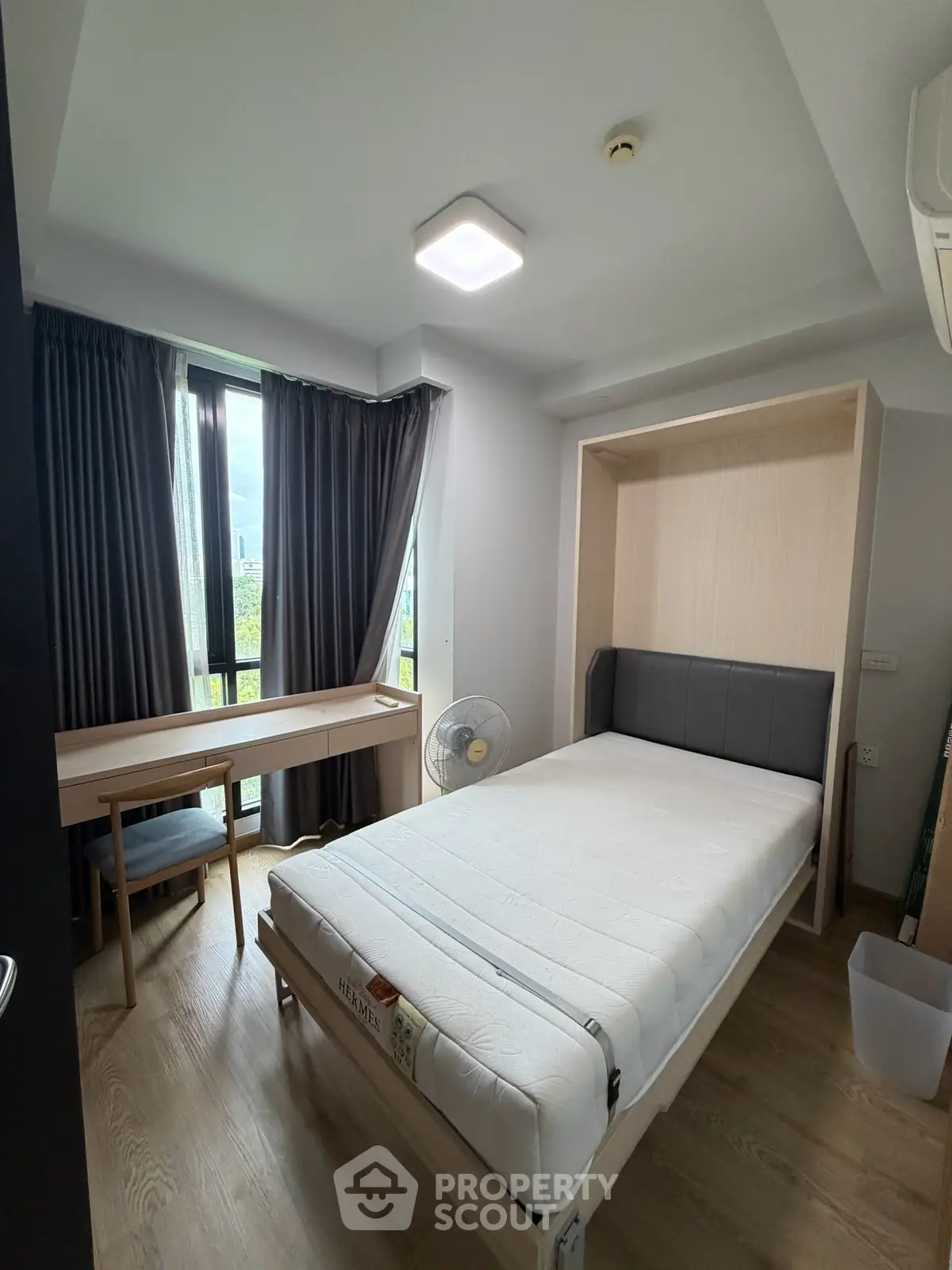 Modern bedroom with natural light, featuring a comfortable bed and study desk, ideal for urban living.