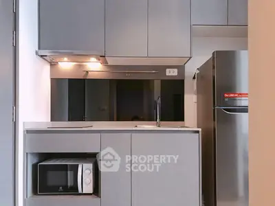 Modern kitchen with sleek cabinetry, built-in microwave, and stainless steel fridge in compact layout.